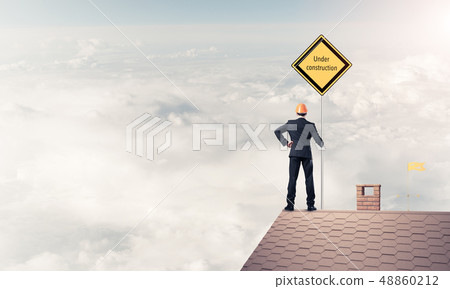 Young businessman on house brick roof holding yellow signboard. 48860212