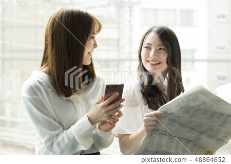 在窗口邊觀看智能手機和報紙的兩名婦女 在窗口邊觀看智能手機和報紙的兩名婦女 48864652