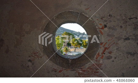 View through a round window in a stone wall 48868860