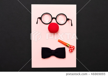 Funny glasses, red clown nose and tie lie on a colored background, like a face. 48869893