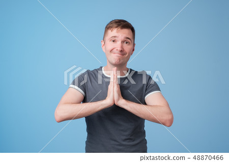 Handsome young man in blue t-shirt pressings palms together begging for forgiveness 48870466