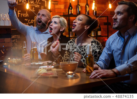 Group of friends watching tv in a cafe behind bar counter 48874135