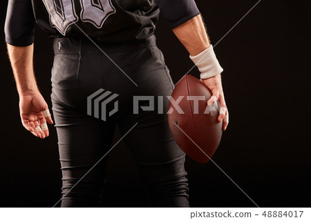 Mid section of American football player with ball against black, copy space, back view Mid section of American football player with ball against black, copy space, back view 48884017