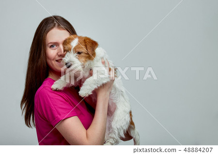 Beautiful girl with a jack russell terrier on her hands on a gray background, copy space 48884207