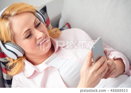 Senior woman at home lying listening to music in headphones happy Senior woman at home lying listening to music in headphones happy 48888915