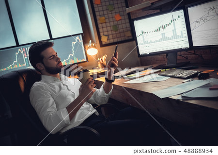 Young male trader at office work concept sitting drinking coffee browsing smartphone 48888934