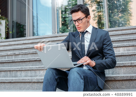 Technology problems. Businessman in eyeglasses sitting on stairs on the city street looking at Technology problems. Businessman in eyeglasses sitting on stairs on the city street looking at 48889991