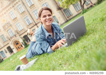 Young student at university campus lying on grass using laptop looking at camera playful 48890299