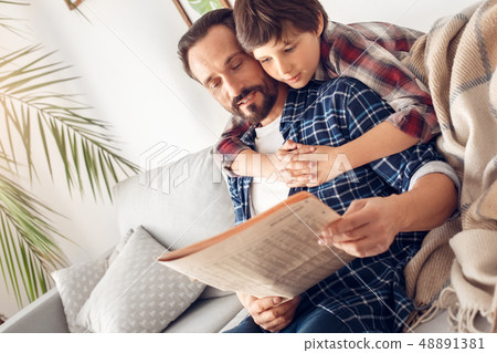 Father and little son at home boy hugging dad sitting on sofa reading newspaper together relaxed Father and little son at home boy hugging dad sitting on sofa reading newspaper together relaxed 48891381