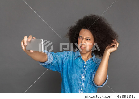 Freestyle. Mulatto woman standing isolated on grey taking selfie on smartphone pouting lips 48891813