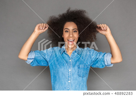 Freestyle. Mulatto woman standing isolated on grey holding hair looking camera playful Freestyle. Mulatto woman standing isolated on grey holding hair looking camera playful 48892283
