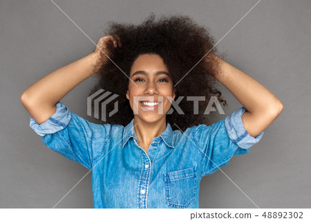 Freestyle. Mulatto woman standing isolated on grey touching hair laughing cheerful close-up Freestyle. Mulatto woman standing isolated on grey touching hair laughing cheerful close-up 48892302