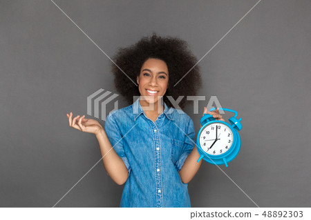 Freestyle. Mulatto woman standing isolated on grey with alarm clock smiling happy Freestyle. Mulatto woman standing isolated on grey with alarm clock smiling happy 48892303
