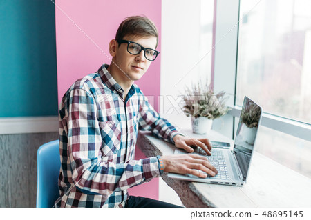 A young man sits in a cafe with a laptop 48895145