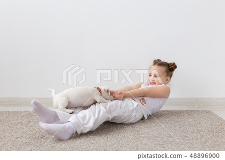 Pet's owner, children and dogs concept - little girl lying on the floor with cute puppy and playing Pet's owner, children and dogs concept - little girl lying on the floor with cute puppy and playing 48896900