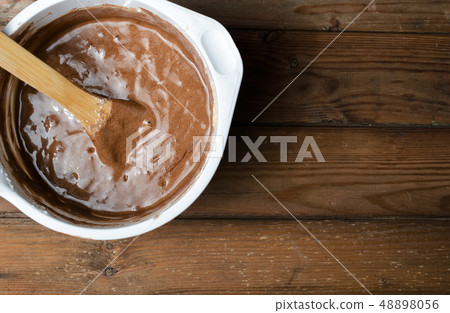 Cake pan with chocolate batter and wooden spoon close up on dark wooden background. 48898056