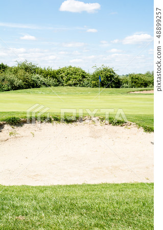 Early summer golf course under blue sky Green flag with a blue flag and a wide open bunker Early summer golf course under blue sky Green flag with a blue flag and a wide open bunker 48899257