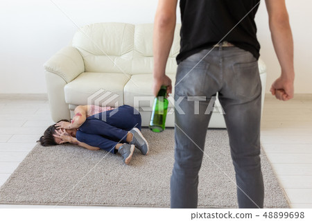 Victim, domestic violence, abuse and alcoholic concept - drunk man with bottle near his wife lying Victim, domestic violence, abuse and alcoholic concept - drunk man with bottle near his wife lying 48899698