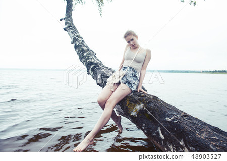 young blond woman hanging on birch tree at lake shore, summer vacations outdoor lifestyle young blond woman hanging on birch tree at lake shore, summer vacations outdoor lifestyle 48903527