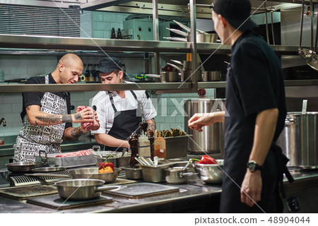 Is it fresh Professional chef in apron holding a red meat and teaching his assistants how to choose Is it fresh Professional chef in apron holding a red meat and teaching his assistants how to choose 48904044