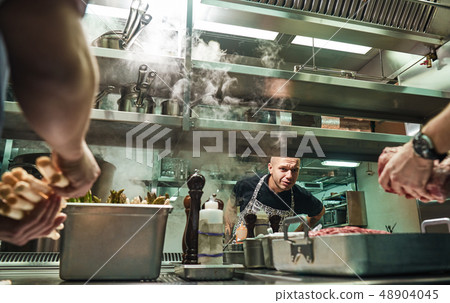 Is everything ok Surious chef is looking how his assistants are cooking a meat in a restaurant Is everything ok Surious chef is looking how his assistants are cooking a meat in a restaurant 48904045