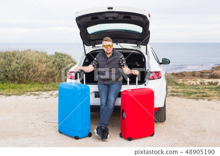 Man standing in back of car smiling and getting ready to go. Young laughing mle standing near open 48905190