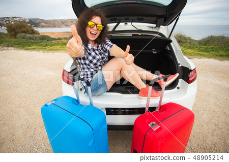 Girl sitting in back of car smiling and showing thumbs up. Young laughing woman sitting in the open 48905214