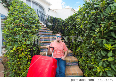 Holiday, travel and tourism concept - Handsome man with red suitcase sitting on a stairs 48905279