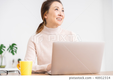 看便攜式計算機的資深婦女在屋子裡 看便攜式計算機的資深婦女在屋子裡 48912314