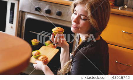 Beautiful blonde woman showing muffins in a kitchen 48916743