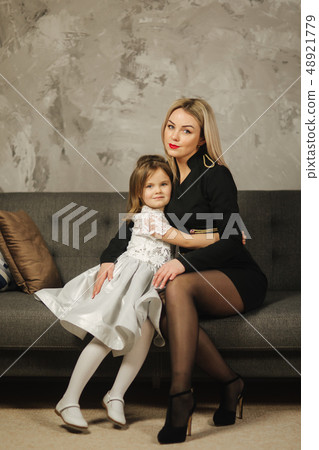Young mom and little daughter at home sitting on sofa. Attractive mother in black dress. Happy 48921779