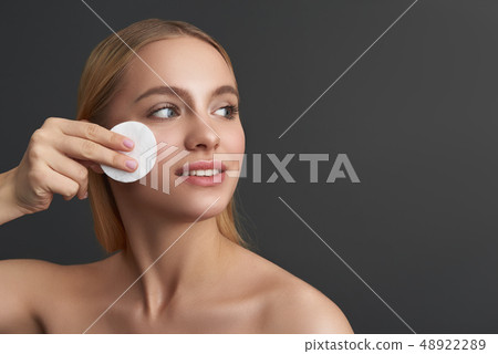 Smiling lady looking away and pressing cotton pad to her face 48922289