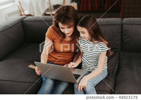 Mother and daughter sitting on sofa with laptop 48923178