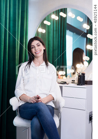 Charming woman sitting on chair at table with cosmetics Charming woman sitting on chair at table with cosmetics 48925144