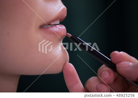 Close up of visagiste's arm applying pencil lip on dark background Close up of visagiste's arm applying pencil lip on dark background 48925256