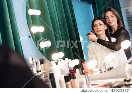 Client's personal stylist applying cosmetics on face in beauty studio Client's personal stylist applying cosmetics on face in beauty studio 48925337