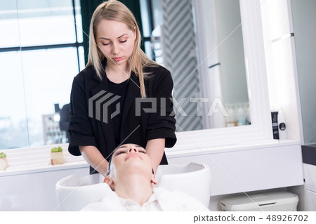 Half length of professional hairdresser making head massage for client in basin Half length of professional hairdresser making head massage for client in basin 48926702