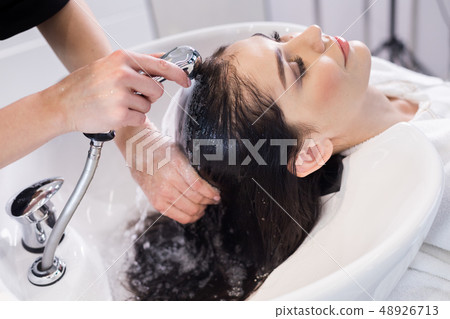Hairdresser washing client's hair in modern basin in hairdressing saloon Hairdresser washing client's hair in modern basin in hairdressing saloon 48926713