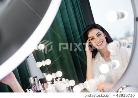 Reflection in mirror of Caucasian brunette woman touching her face with arm 48926730