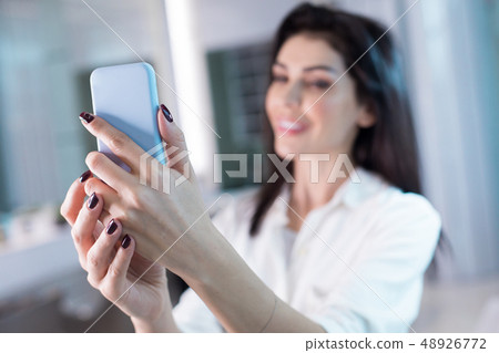 Smiling lady holding cellphone in arms in hairdressing saloon Smiling lady holding cellphone in arms in hairdressing saloon 48926772