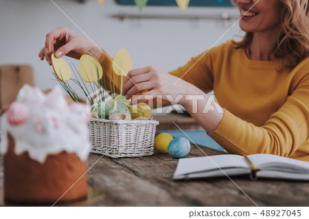 Happy woman decorating Easter basket with eggs Happy woman decorating Easter basket with eggs 48927045