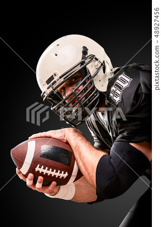 Portrait of American football player holding a ball with both his hands Portrait of American football player holding a ball with both his hands 48927456