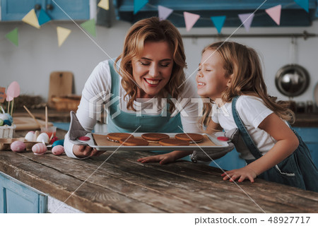 Little girl with mom smelling delicious cookies Little girl with mom smelling delicious cookies 48927717