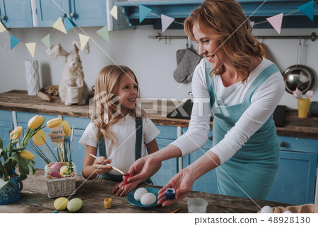 Happy mother and daughter coloring eggs at home 48928130