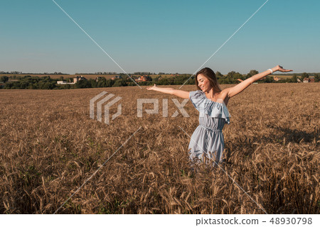 A beautiful and young girl is standing in a summer wheat field. Arms outstretched happy smiles A beautiful and young girl is standing in a summer wheat field. Arms outstretched happy smiles 48930798