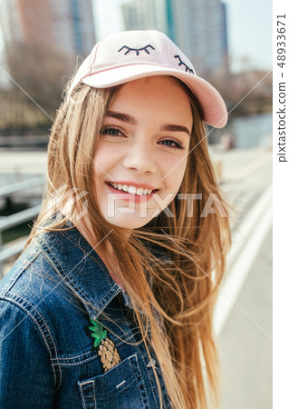 Portrait closeup beautiful young girl in pink hat in city street 48933671