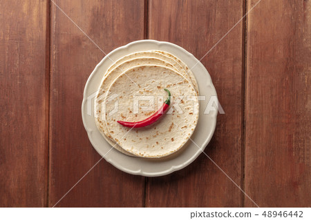 A red hot chilli pepper, shot from the top on a pile of tortillas, Mexican flatbreads, on a dark 48946442