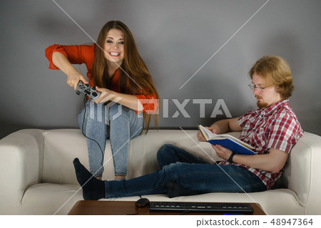 Woman playing games man reading book Woman playing games man reading book 48947364