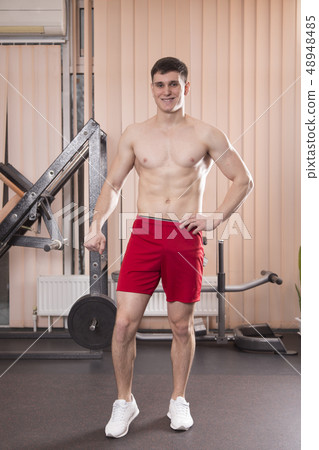 Young man flexing muscles with barbell in gym. 48948485