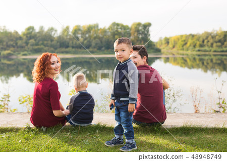 Childhood and nature concept - Family with little sons sitting on the green grass Childhood and nature concept - Family with little sons sitting on the green grass 48948749